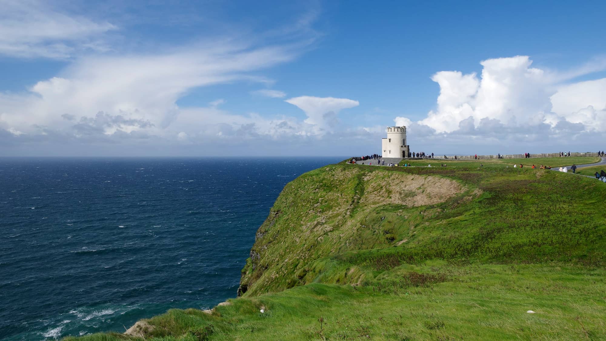 Grassy sea cliffs above the dark blue Atlantic with O'Brien's Tower in the distance